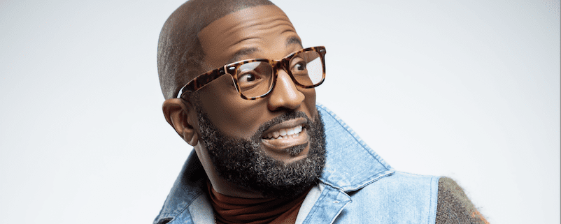 Man with glasses and denim jacket smiling.